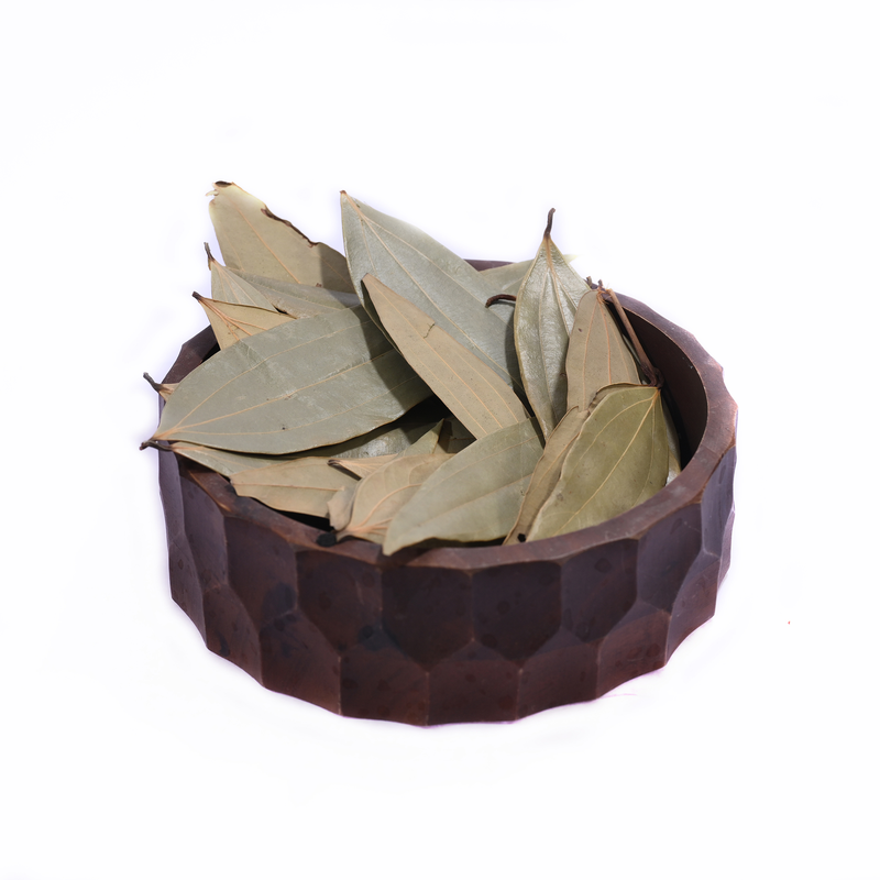 A wooden bowl holding dried bay leaves, branded with a label from House of Rasda