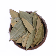 A bowl of dried bay leaves on a wooden kitchen counter, with a House of Rasda product label beside it