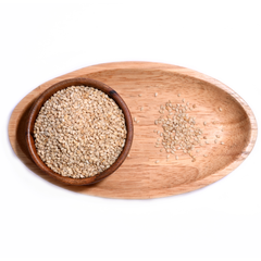 Wooden Bowl filled with white sesame seeds, some seeds spilling out onto a wooden table